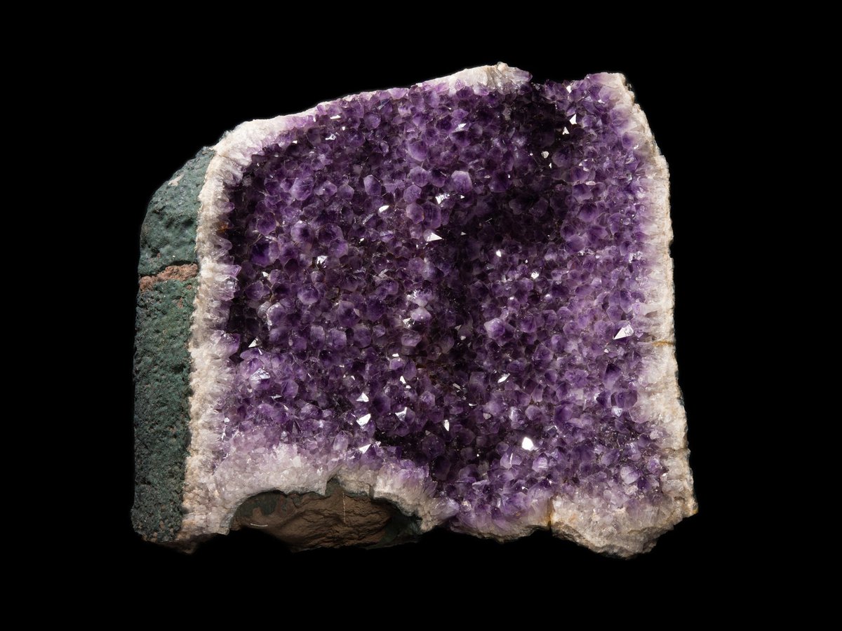 Cross-section of a deep purple amethyst geode lined with crystals in basalt rock